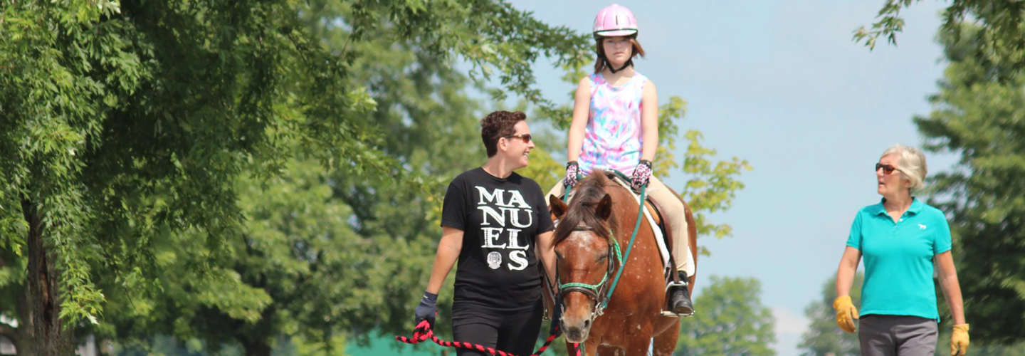 Une jeune fille accompagnée de deux adultes monte un cheval.