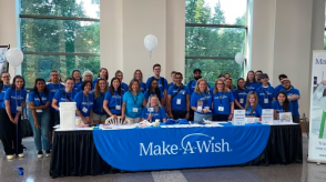 A group of make-a-Wish volunteer pose behind a table for a picture. 