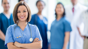 A doctor with a stethoscope poses in the foregrounbd while her colleagues are in soft focus in the background. 
